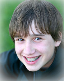 young teenage boy with braces sitting on the grass and smiling