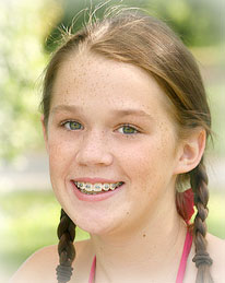 young girl with braces sitting on the grass and smiling